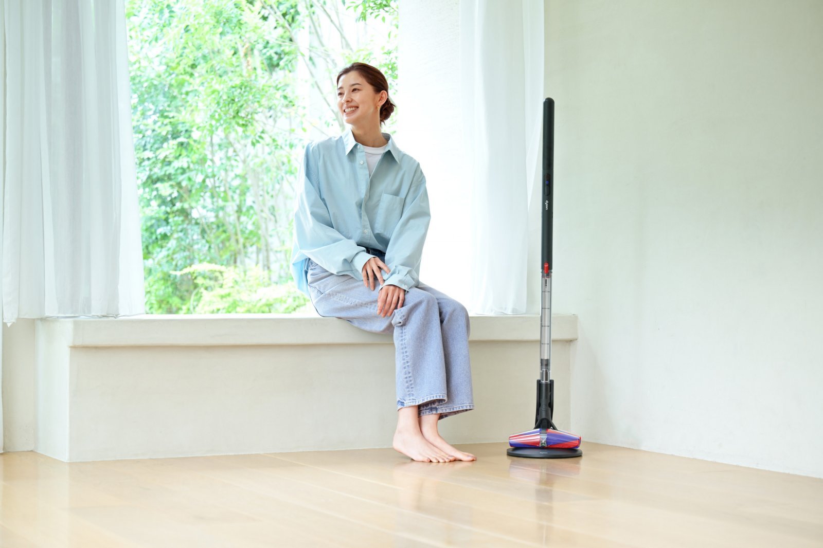 窓辺に座っているモデル・女優の朝比奈彩さんとその隣に置かれたダイソンの掃除機pencilvacfluffyconesTMクリーナーヘッドの画像。